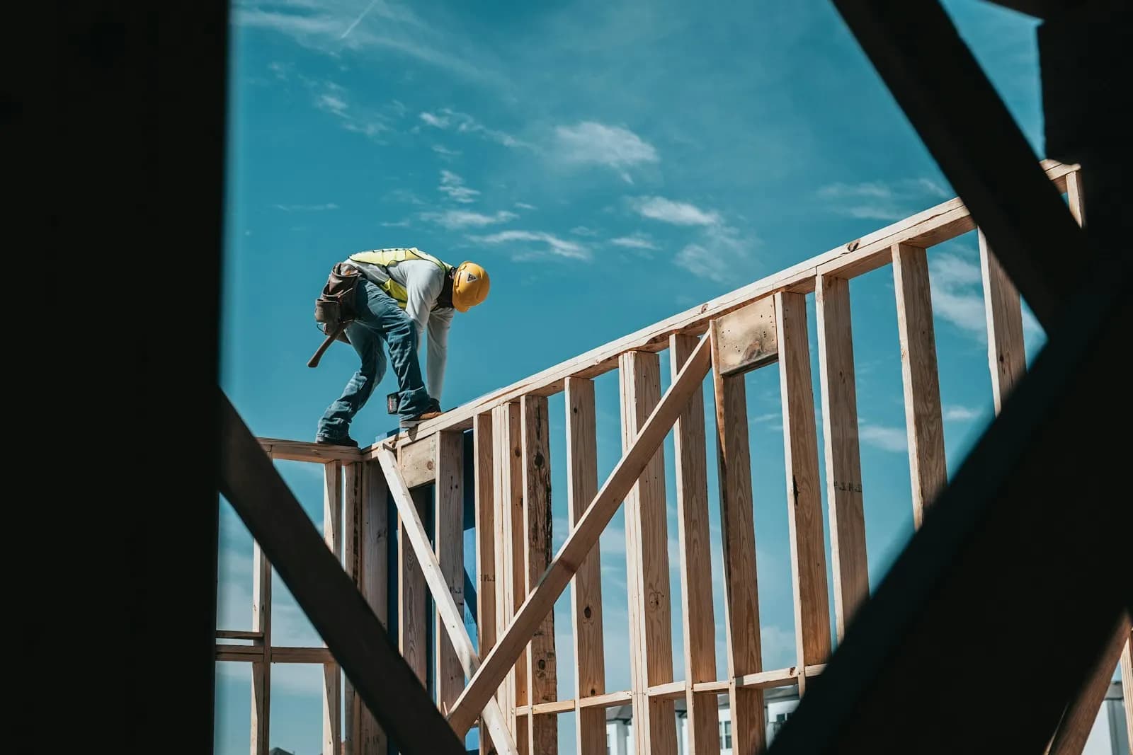 A framer walking the top plate of a wood-framed house against a blue sky